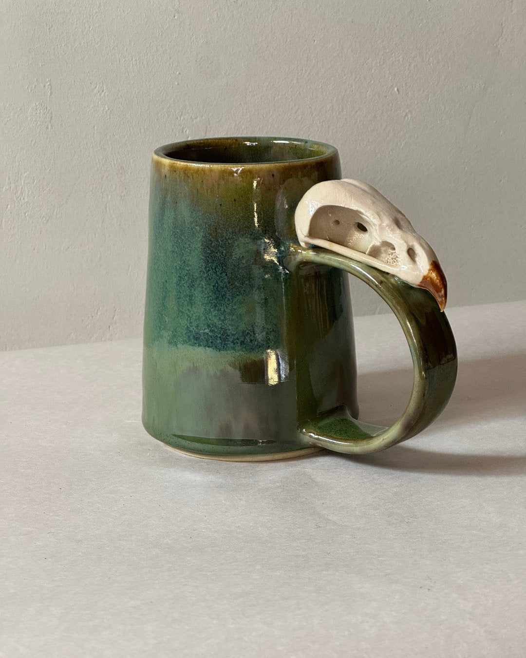 Green and brown mug with ceramic hawk skull on the top of the handle