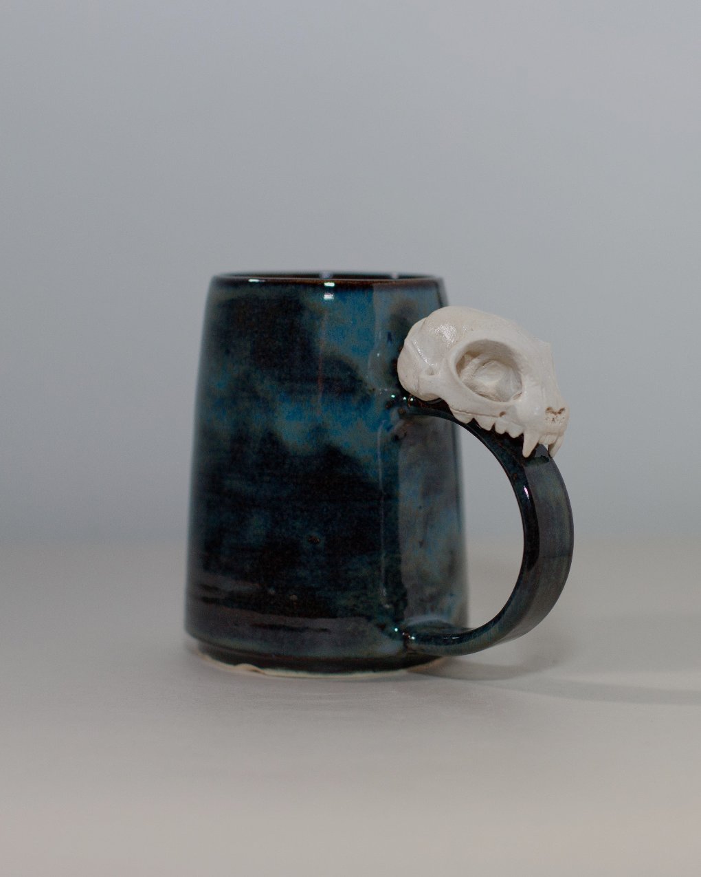 rust colored ceramic mug with ceramic cat skull attached to the handle