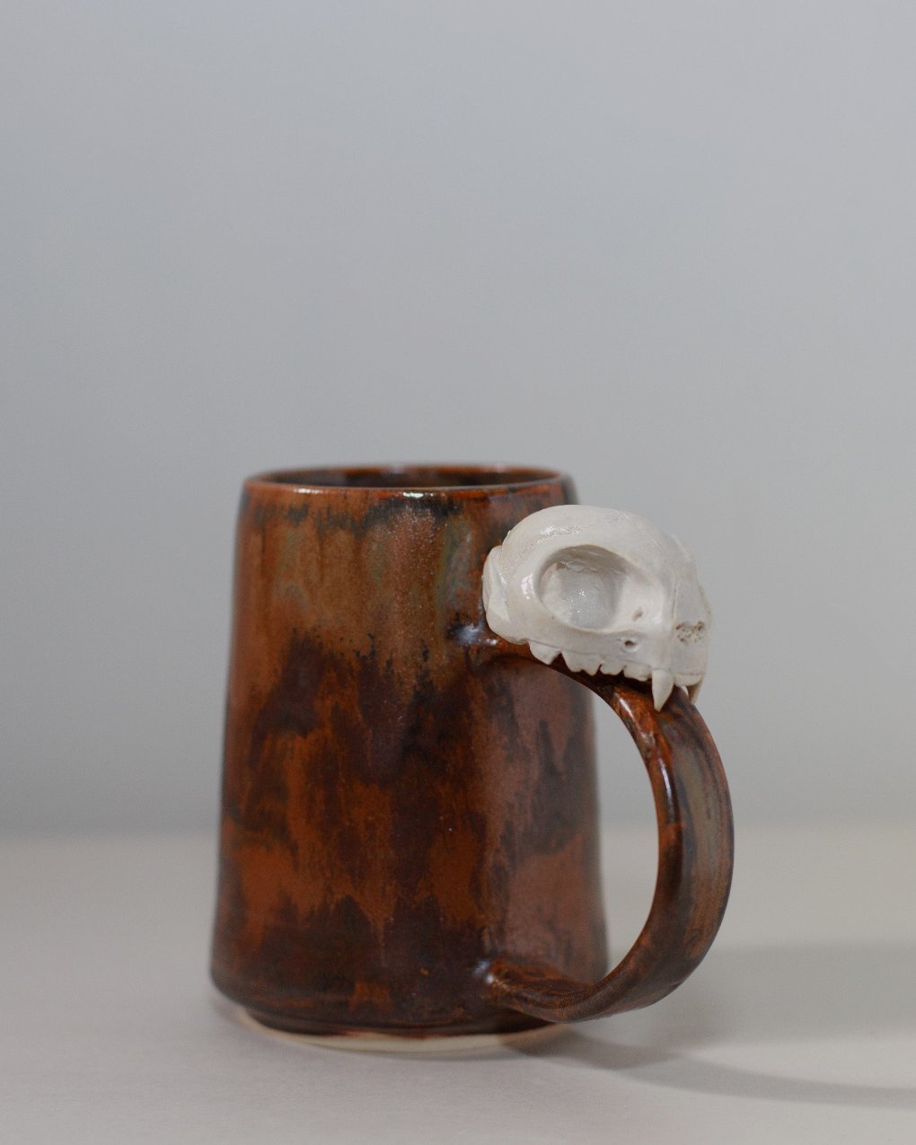 rust colored ceramic mug with ceramic cat skull attached to the handle