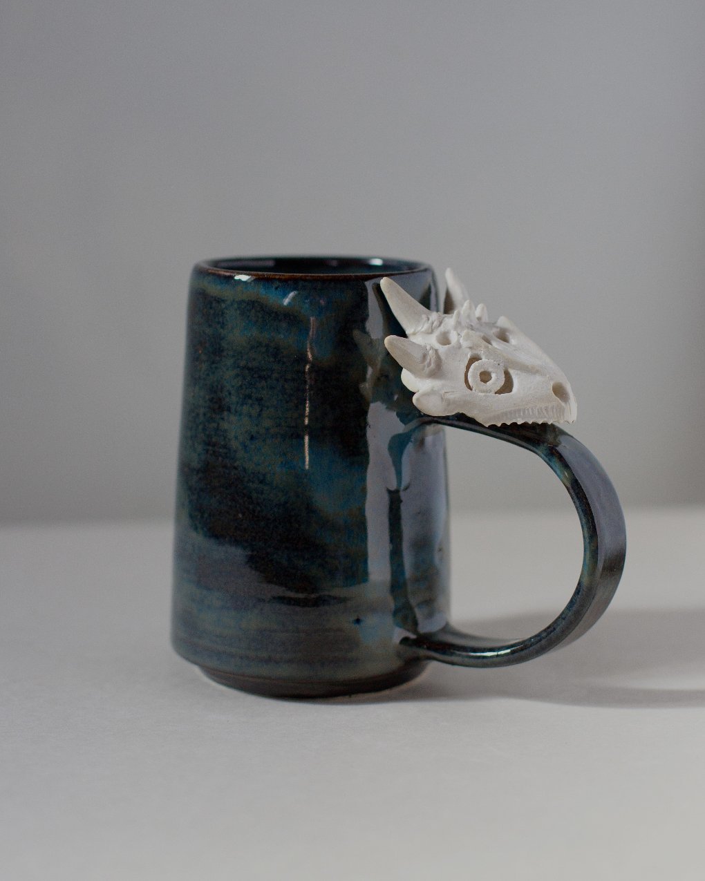 rust colored ceramic mug with ceramic lizard skull attached to the handle