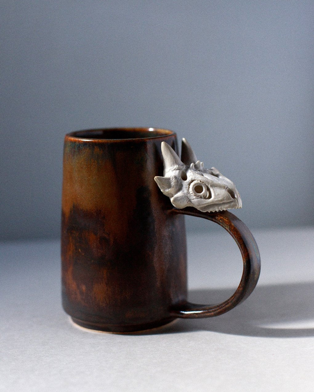 rust colored ceramic mug with ceramic lizard skull attached to the handle