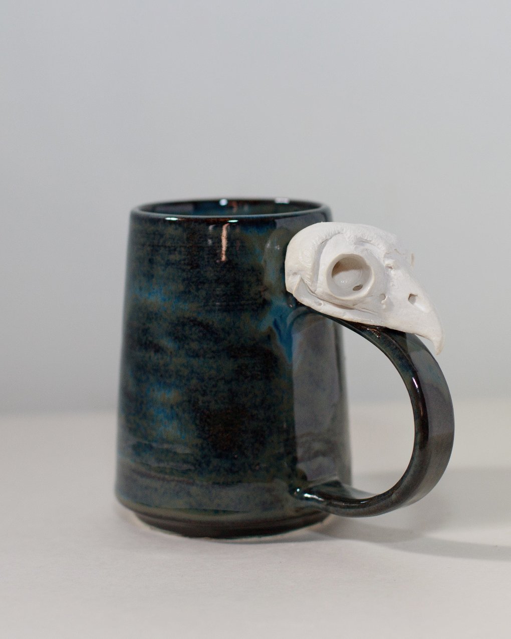 rust colored ceramic mug with ceramic owl skull attached to the handle