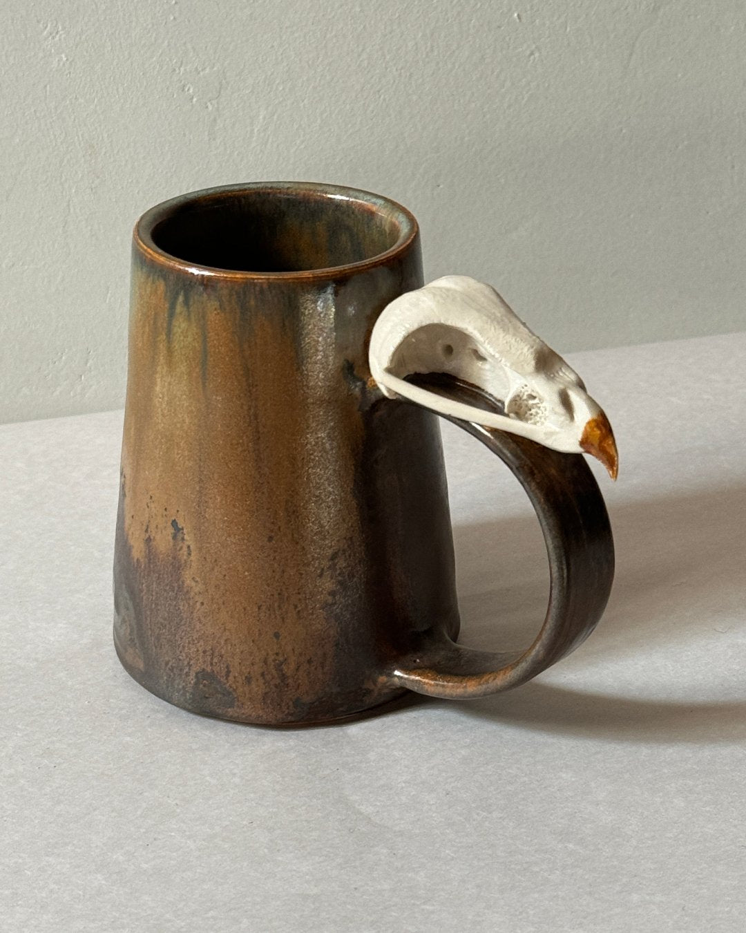 brown and orange mug with ceramic hawk skull affixed to the handle