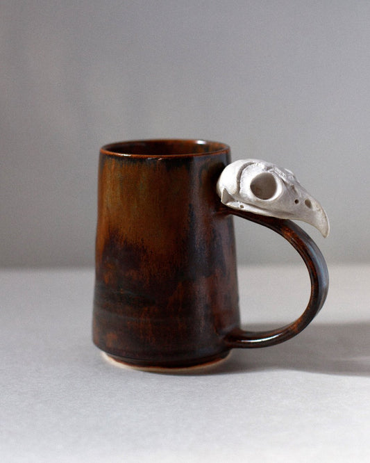 rust colored ceramic mug with ceramic owl skull attached to the handle