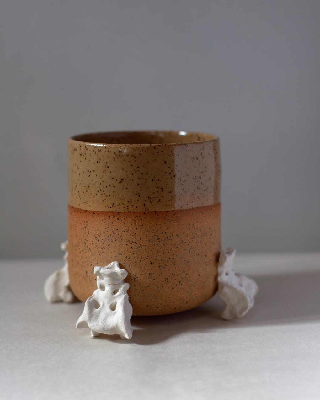 Handmade two-tone ceramic planter with a matte and gloss glaze, supported by three hand-sculpted ceramic replicas of raccoon sacrum bones, displayed on a neutral background.